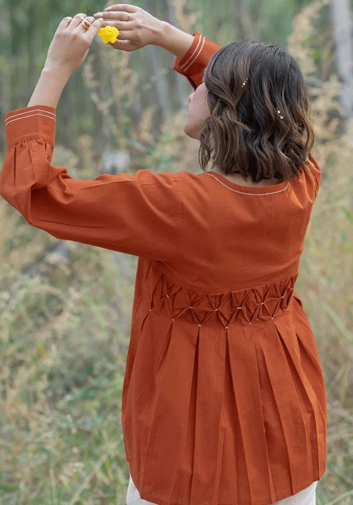 A woman in an orange top with a round neckline, full sleeves, and a front button