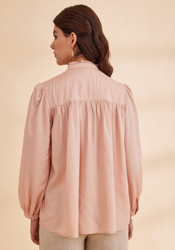 A woman wearing a pink top with floral embroidery at the yoke, full sleeves, and a round neckline.