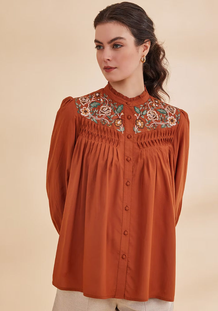A woman wearing a Rust top shirt with full sleeves, floral embroidery at the yoke, and a round neckline with a band collar.