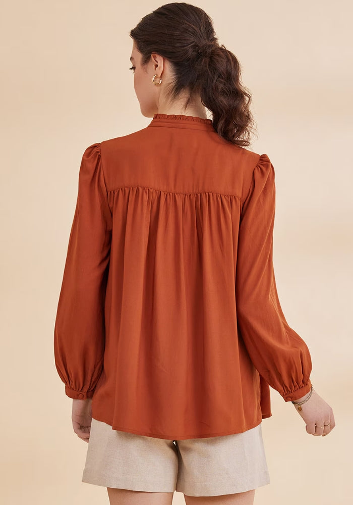 A woman wearing a Rust top shirt with full sleeves, floral embroidery at the yoke, and a round neckline with a band collar.