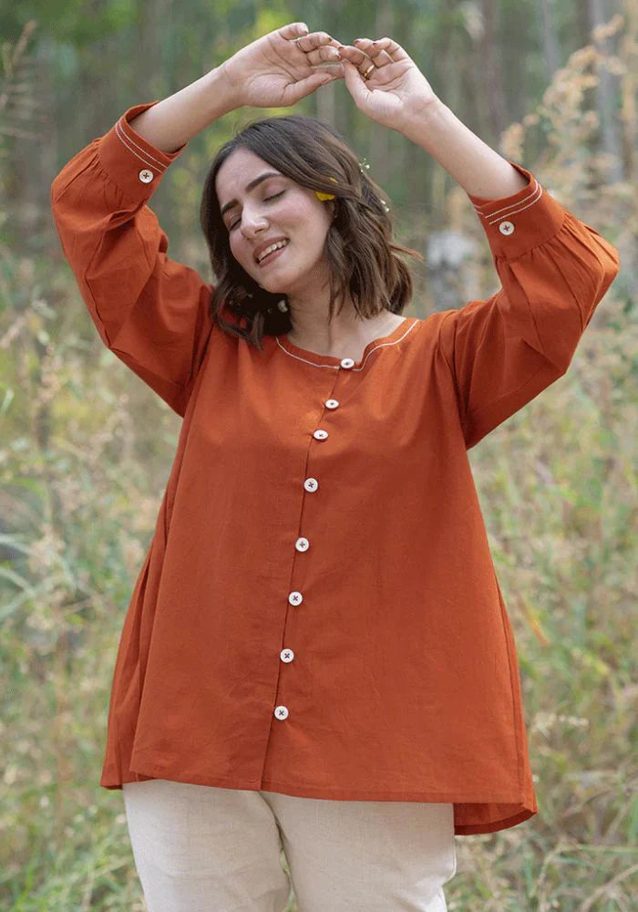 A woman in an orange top with a round neckline, full sleeves, and a front button
